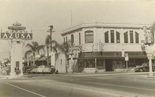Looking at the NW corner of Route 66 and Azusa Ave. Azusa CA 1940s black and white, street crosses US66, sign reads AZUSA atop a column on the left, and a drugstore on the corner to the right, cars parked palm trees on sidewalk. Azusa c.1940s