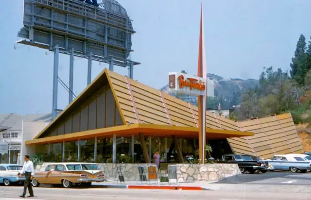 A frame building, canted roof, large windows, neon sign, cars