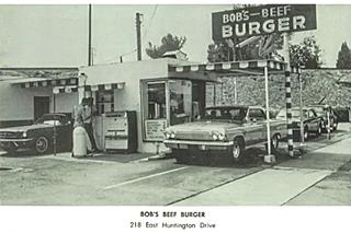 Bob’s Hamburgers, 1960s Arcadia black and white hamburger drive-in, Bob’s, car, sign above small box-shaped building flat canopies, people