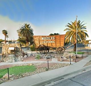 a borax wagon on a plaza, with palm trees and words NEEDLES CALIFORNIA written on it