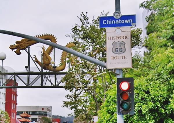Historic US66 alignment sign in Chinatown Los Angeles CA Route 66 yellow dragon on archway over street, a sign with HISTORIC US 66 ALIGNMENT on the right by a traffic light under blue sign reading CHINATOWN