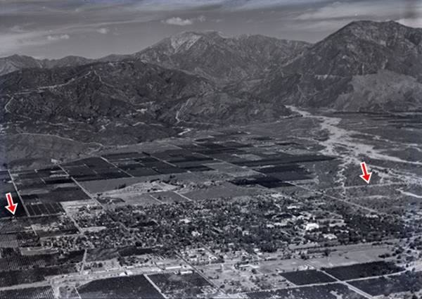 black and white 1939 aerial photo of town, mountians on the top, fields with orchards around city on the bottom, red arrows mark US66