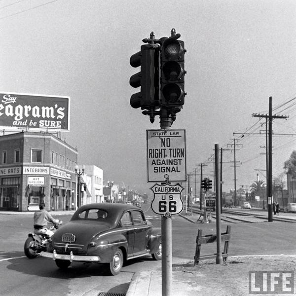 1948 US66 in Beverly Hills black and white car turning on traffic light, US 66 shield, building and billboard
