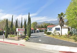 color, 2021, motel with cabin like units seen from US 66, mountains beyond. Sign and some cypress trees by the highway