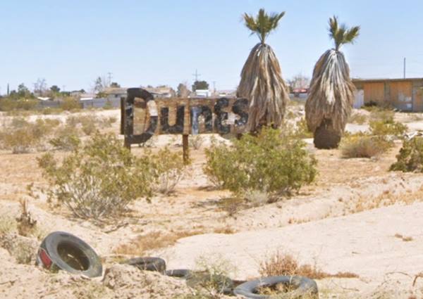 yuccas, litter and tires, DUNE sign, vacant building beyond, arid desert