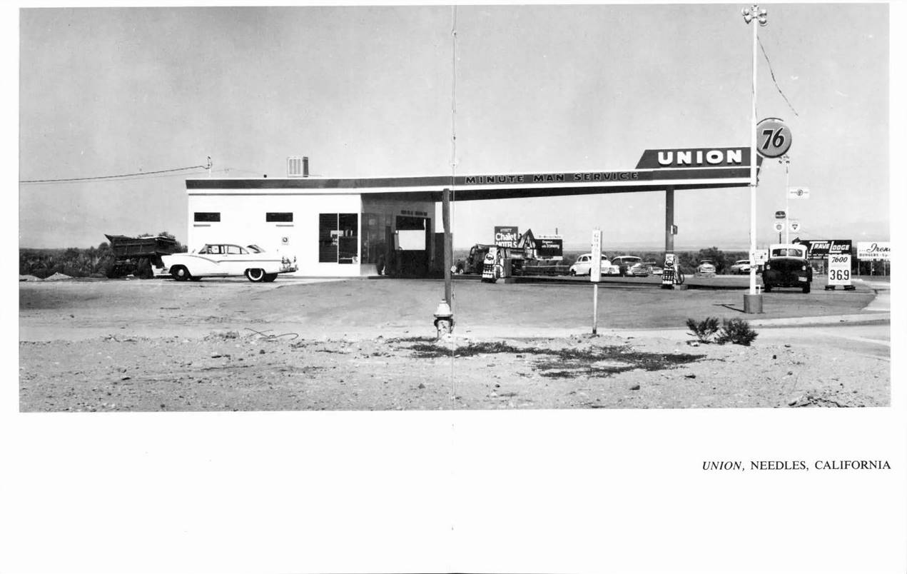 black and white photograph of a Union gas station with a large long flat canopy, cars and gas pumps, 1962. Needles