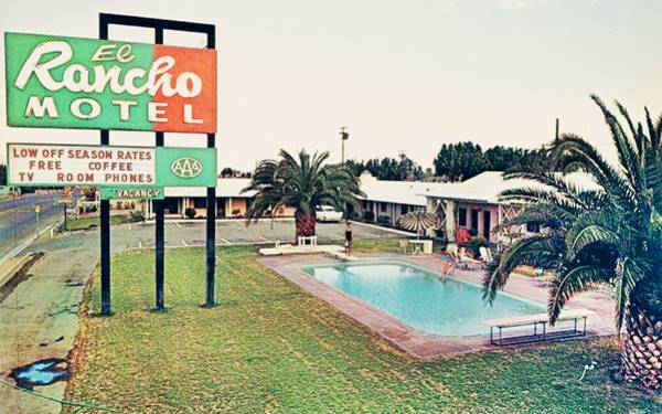 El Rancho motel, color. L-shaped layout, central pool by palm trees and the neon sign