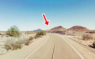 dry arid area, some hills in the distance, highway running towards them, junk and some trees to the left