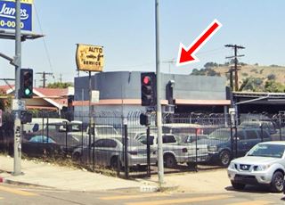 color. Gray building on a corner behind black fence, with cylinder shaped office, bays to both sides, former station, cars parked. Sign reads AUTO SERVICE