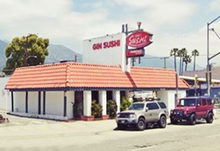 corner building, faux-tiled roof around a flat rood building with vertical wall perpendicular to highway with name of restaurant, and red sign next to it