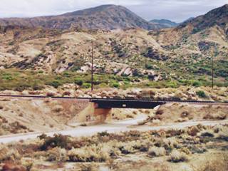 color, shrub-covered rugged terrain, railway crosses over a dirt road with a short viaduct