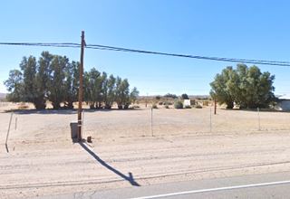 empty sandy plot of land, US66 in front, trees behind