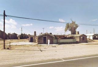 round grey stone building, gable roof, single story, US66 in front, trees behind
