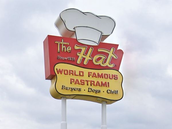 1950s styled retro neon sign topped with a cook’s hat, upper panel red with yellow letters: THE HAT SINCE 1951; bottom yellow panel rounded says: WORLD FAMOUS PASTRAMI BURGERS.DOGS.CHILI