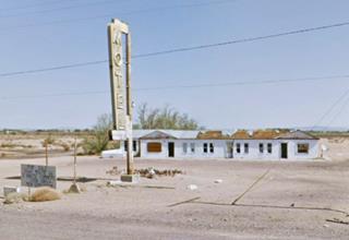 Henning Motel in 2011 single story gable roof motel, vacant, gravel drive, bushes, hills beyond and neon sign in foreground by US66