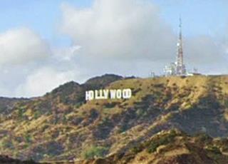 color, white capital letters spell HOLLYWOOD on the slope of a hill with shrubs