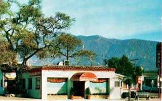 vintage color postcard, building on corner, Chinese look, single story, tree to the left, mountains beyond. Sign on the right