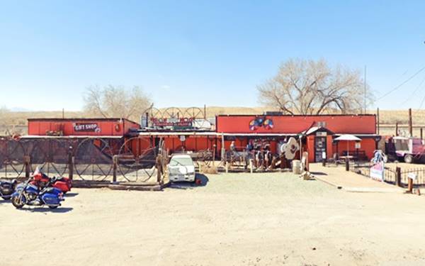 saloon painted orange-red, single story, long, with many memorabilia items in front of it: giant guitar, Evil Knievel bike sign etc. Seen from Route 66