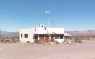block shaped bldg. single story, windows boarded, vacant, hills in the distance, pole of neon sign, empty