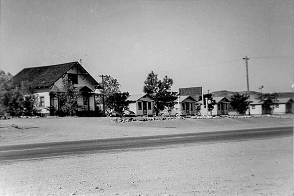 Ludlow Motel and Post Office 1940. black and white 1940. Cottage 2 story building left, motel sign right and 5 cabins, 2 cars parked by them and trees. US 66 runs in front