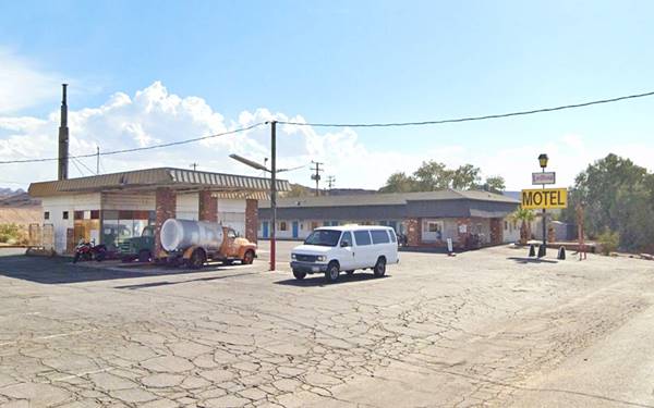 US 66 left: gas station, brick veneer, orange truck under flat canopy. Right: motel, mansard roof, yellow sign reads MOTEL, trees and US66