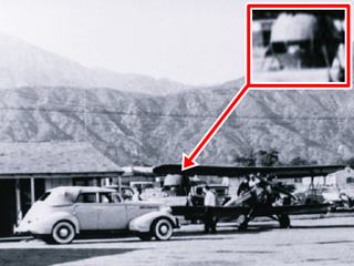 McDonalds orange juice stand 1940s Monrovia US66 1940 black and white photo airport scene, car, planes, orange juice stand shaped like giant orange in the distance. Mountains beyond