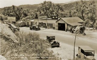 Meeker’s original site 1927 sepia, US 66 curves by gas station and store, 1920s cars, trees, rugged terrain