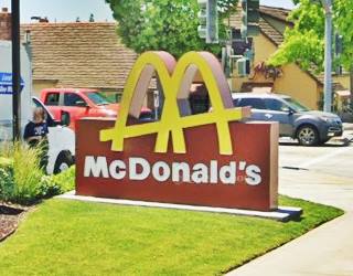 McDonalds sign on sidewalk, with two arches crossing each other forming an M and a slash across both