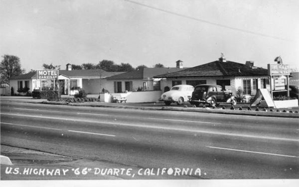 1930s Motel Zanzibar and The Filly Motel Duarte CA Route 66 black and white 1930s. on the right, neon sign of THE FILLY MOTEL, hip roof building and 2 cars parked there. To the left: ZANZIBAR MOTEL with sign and single story hip roofed buildings. Route 66 runs across the image in front of the buildings