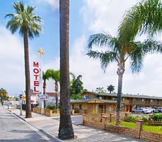 former Ken Lin motel nowadays San Bernardino palm trees white neon sign red letters spell MOTEL. Gable roof and canopy. 2 stories, cars parked