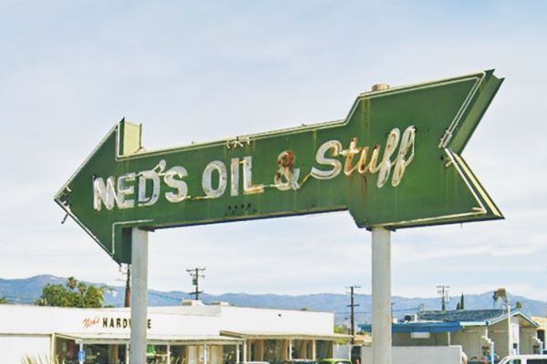 neon sign shaped like a green arrow with white letters reading NED’s OIL & STUFF.