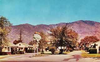 New Salem motel 1950s Monrovia US66 1950s color photo motel with U-layout, gable roofed, trees around it and in center of courtyard. Mountains behind