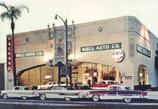 color 1950s postcard 3 cars parked by ornate building with large glass windows, palm tree, neon sign is lit