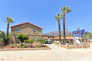 gable roof 2 story building left, neon sign blue and white right, more gable 1 story units to the right, palm trees, mountains beyond