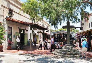 Olvera Street nowadays, Los Angeles color current. People in a pedestrian street with trees, Spanish-Mexican buildings, stores. Cross to the right by tree