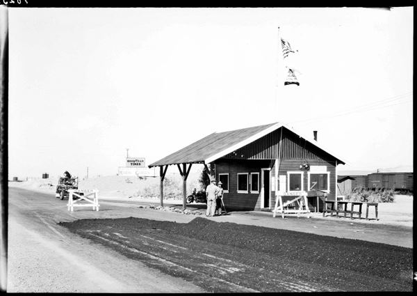 Daggett original inspection station 1930s US 66 black and white 1930s, men by gable roof inspection station, US66 being paved, sign to the left says DAGGETT MODERN CABINS, railroad behind