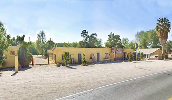 pale yellow buildings: left perpendicular to Rte 66, middle: facing highway, both flat roofed. Right: gable roof, by palm tree. Al single story, former motel US66 runs in front