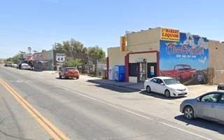 stores, right one with mural, further left a US 66 shield, facing Route 66, cars, blue sky