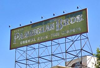 green sign faded, with weathered white letters reads "Pashgian Bros. Oriental Rugs · Fine Carpets"