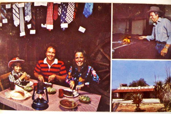 Pinnacle Peak vintage postcard, San Dimas Route 66 vintage colored postcard shows man, woman, child eating on checkered tablecloth under hanging ties. Man cooking steak, and building with steer on roof