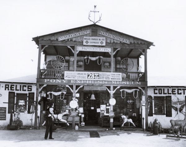 Pony Express Museum 1939 Arcadia CA Route 66 black and white, 1939, man standing by 2 story Western style woodframe building with signs about Wild West Relics, W. Parker Lyon, Pony Express Museum, topped with elk horns