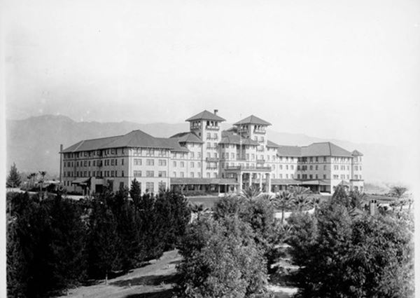 1902 Raymond Hotel, South Pasadena CA Route 66 black and white 1902 photo, building with hip roofs, and wings, massive, four and five stories, verandah, turrets on each side of main portico, mountains beyond, trees around it