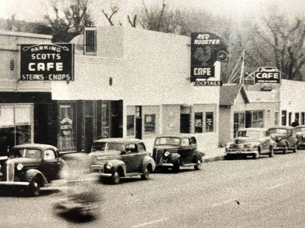 black and white, 1930s, cars parked along sidewalk, cafes line it, Red Rooster, Scott’s and Freds