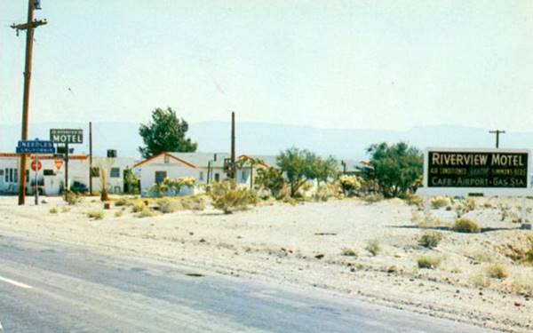 palm trees, US 66 in front sign indicates RIVERVIEW MOTEL CAFE GAS, cabins with gable roofs on the right, one beside the other, gas station to the left