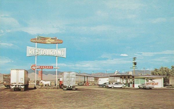 Roadrunner 1960s US 66 color 1960s postcard, trucks and cars parked at a cafe and gas station, 2 buildings flat canopy station, hills beyond, neon sign tall, 2 steel poles reads ROADRUNNER RESTAURANT
