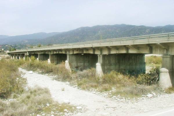 color, 2020s, concrete piers and bridge seen from gravelly area with bushes below it, Mountains in the distance