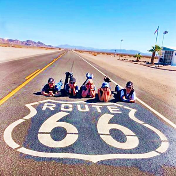 5 persons lying on roadway next to US 66 shield painted on the pavement