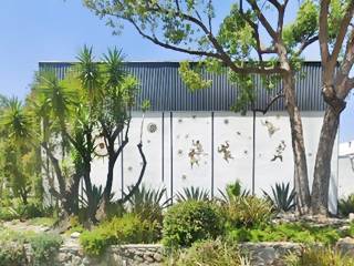 white walls of a building with brown figures painted on it, lush plants and trees frame the scene