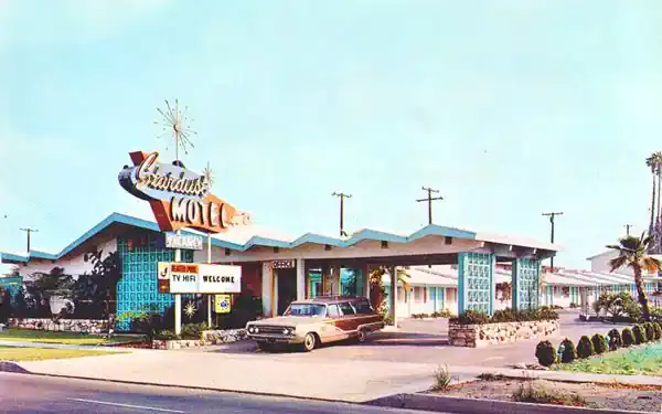 Stardust Motel in a 1960s postcard station wagon late 1960s drives out under motel canopy with saw-tooth roof, space age neon sign with stars announces Stardust Motel. Photo postcard