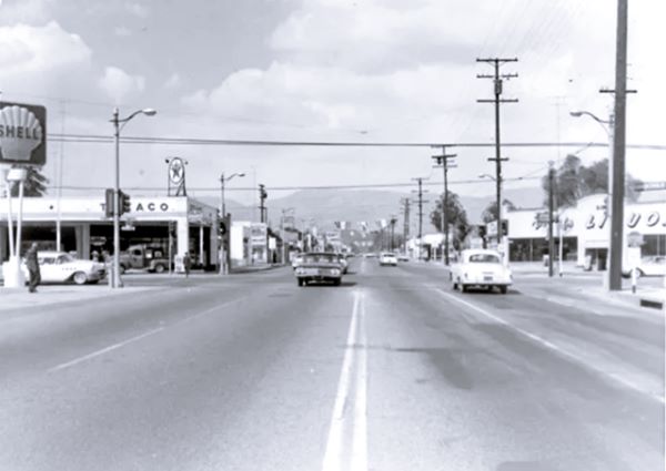 1960s street scene at Mt Vernon and 5th St San Bernardino black and white early 1960s intersection Shell and Teaco to the left, mountains in the distance, cars, signs, Liquor store right